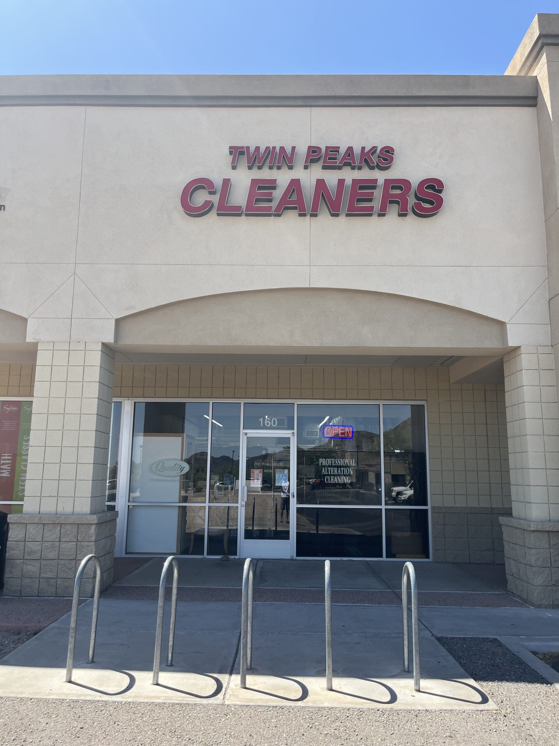 The exterior of Twin Peaks Cleaners, with a glass door, large windows, a bike rack, and an
